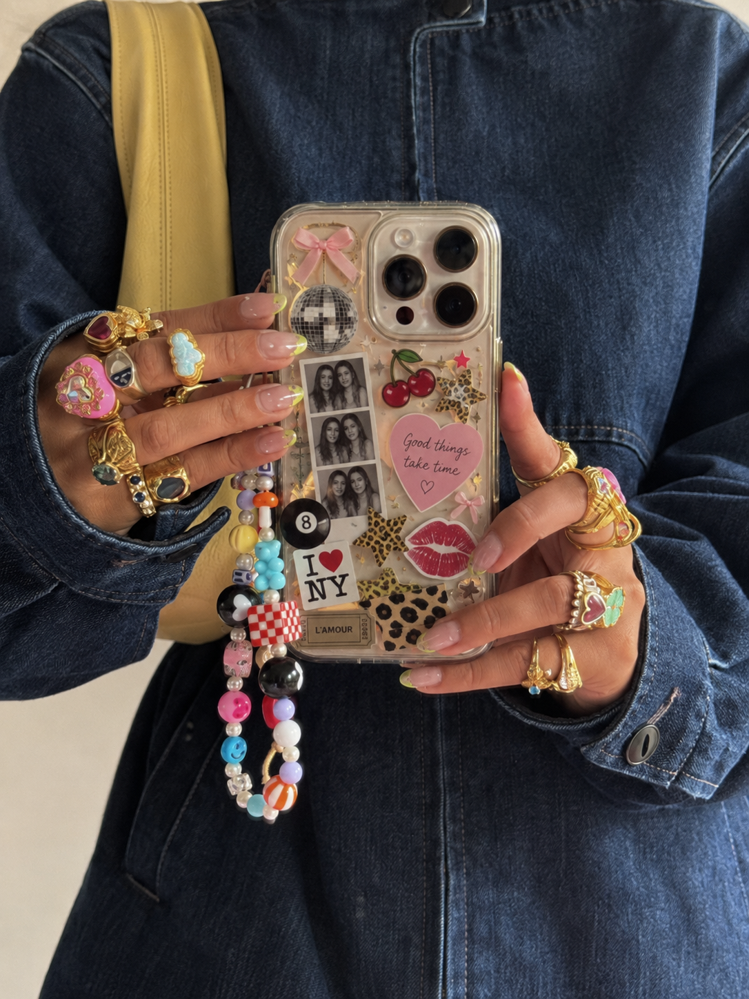 Hand met ringen houdt een telefoonhoesje vol stickers en postzegels vast, met een kralenkoord